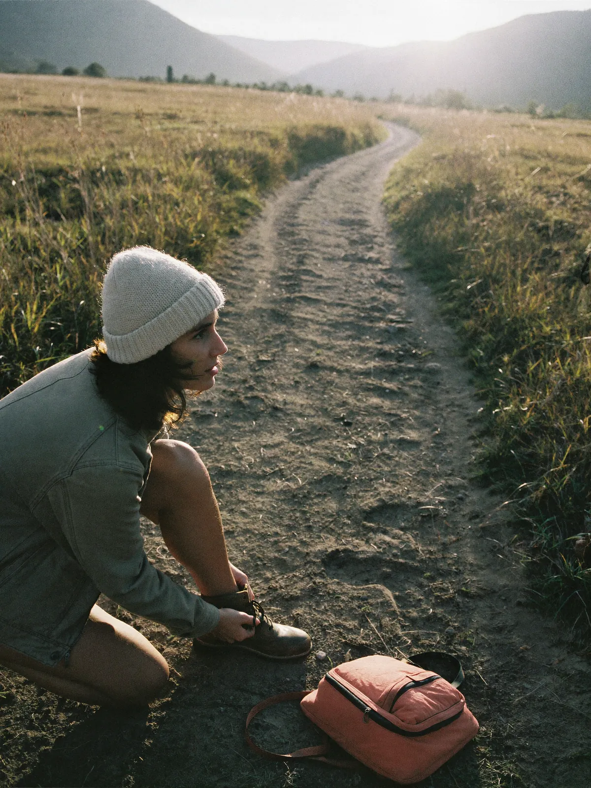 A person ties a walking boot at the start of a meadow trail at sunrise